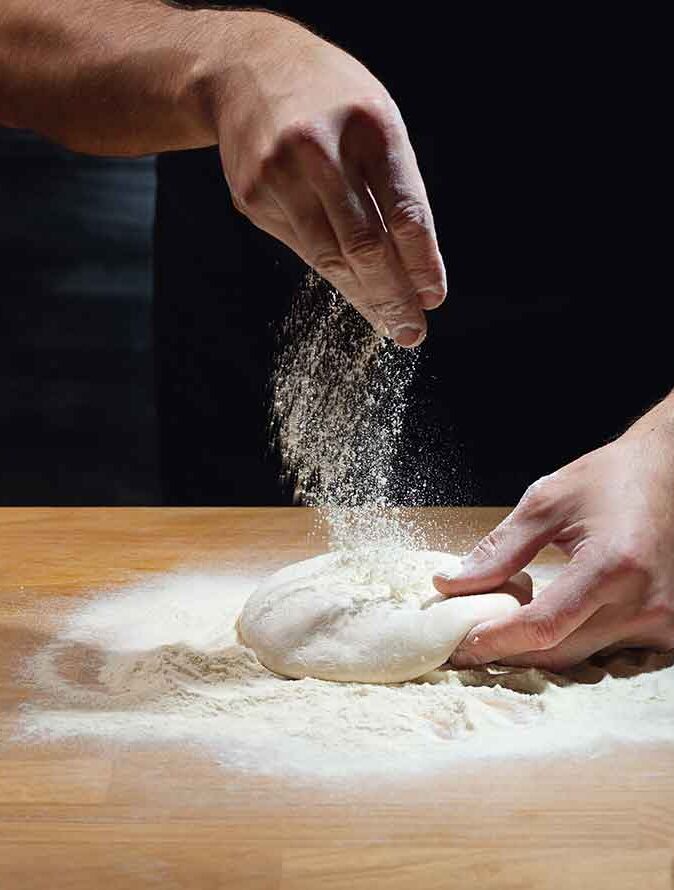 Mehl wird über Pizzateig gestreut